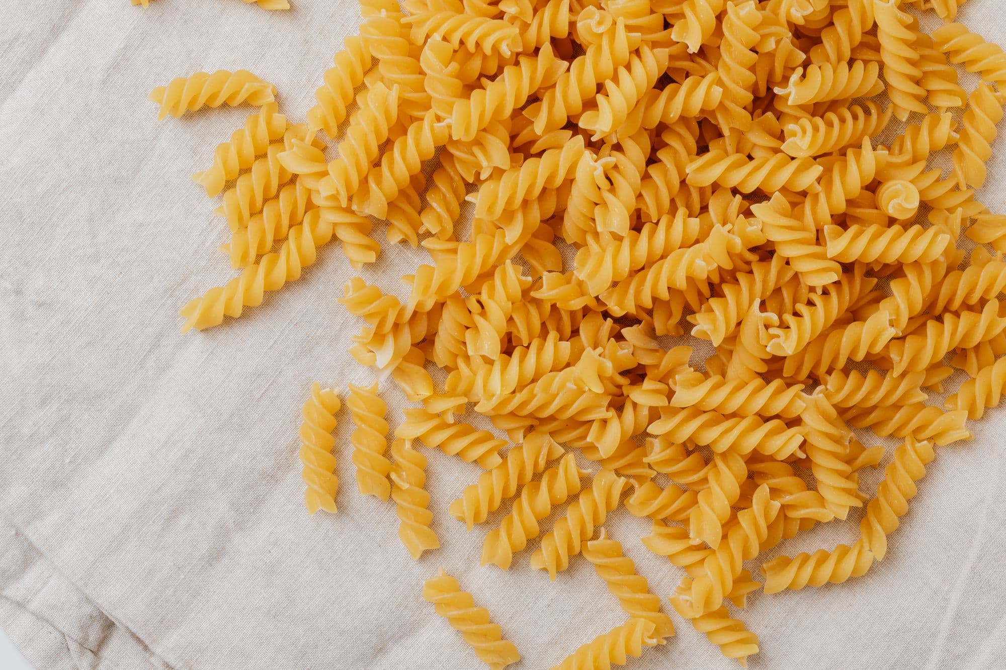Dried fusilli corkscrews scattered across pale linen