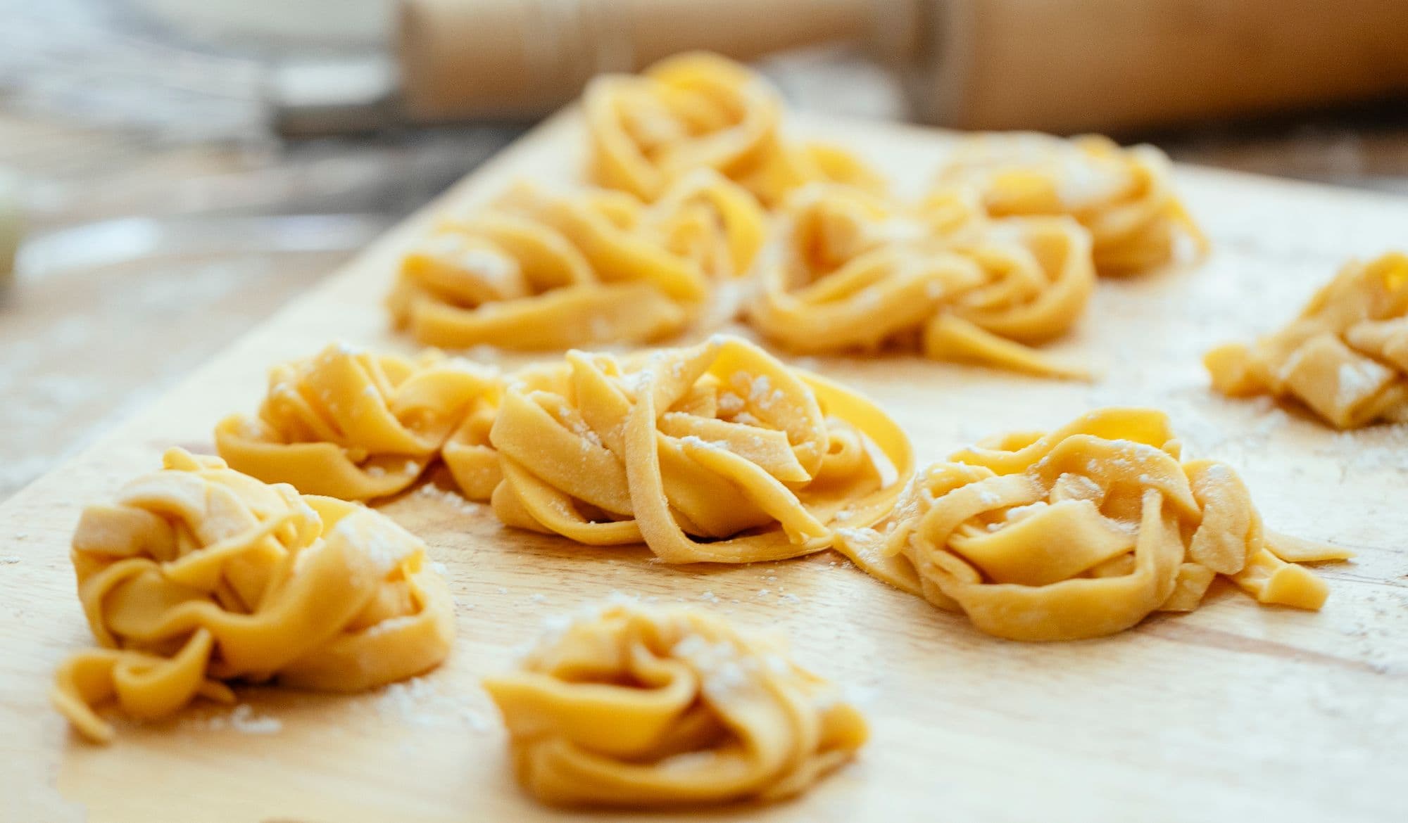 Nests of fresh tagliatelle egg ribbons dusted with flour on a wooden board